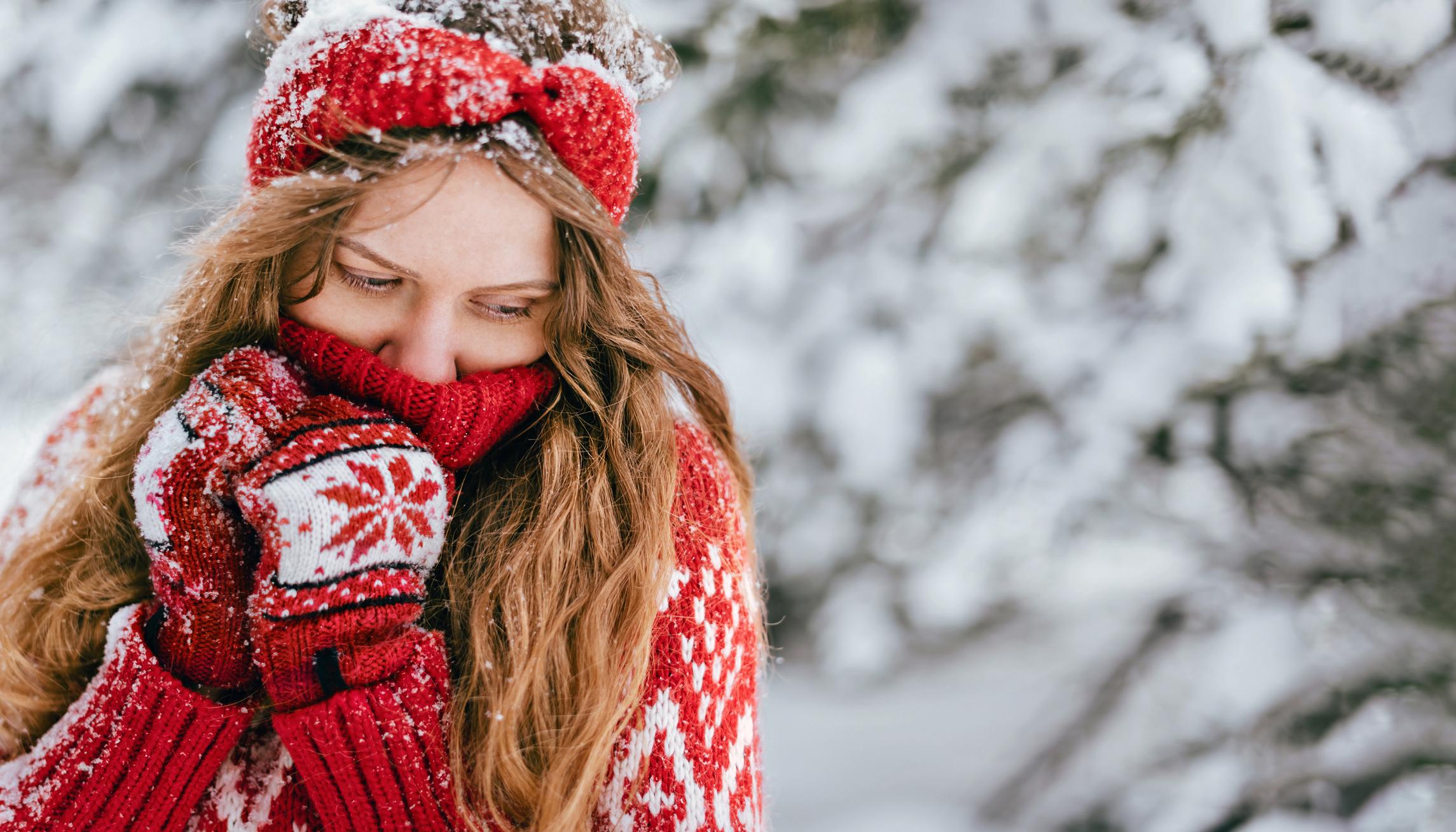 Woman wearing handmade red knitted winter sweater, scarf and gloves in snow